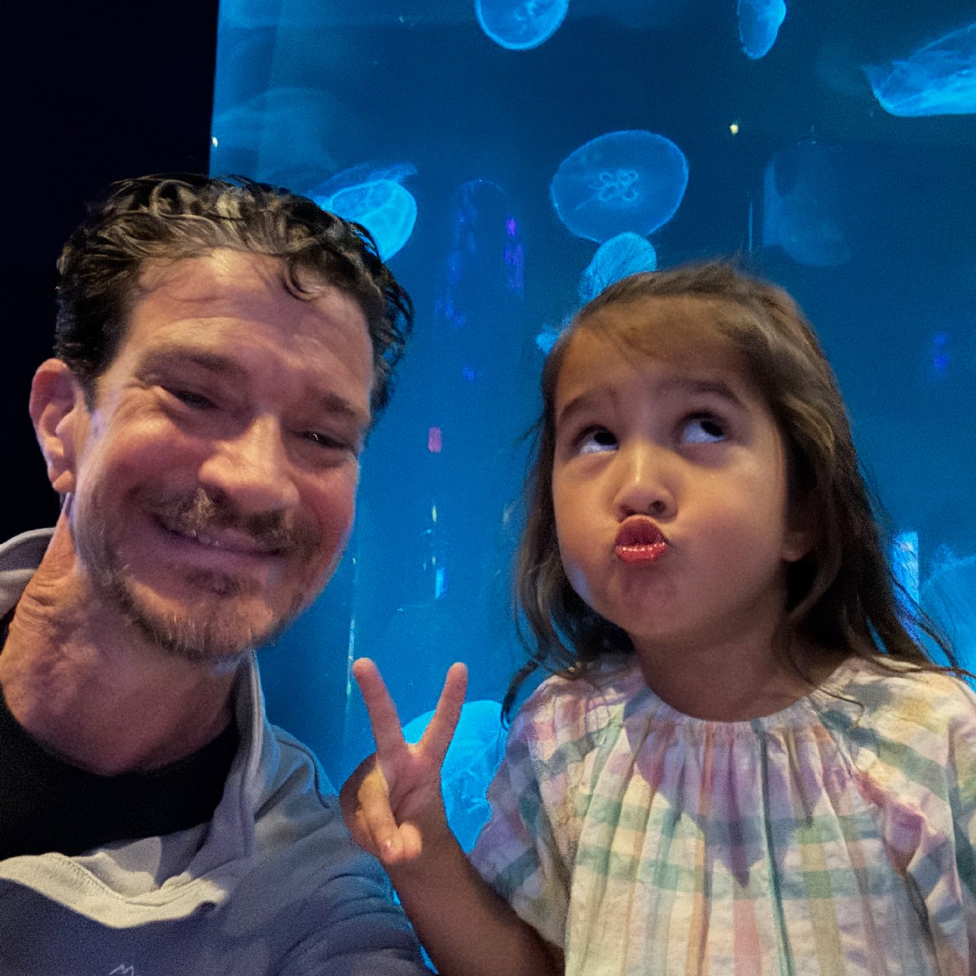 Erik and his granddaughter Hazel making faces in front of a jellyfish tank