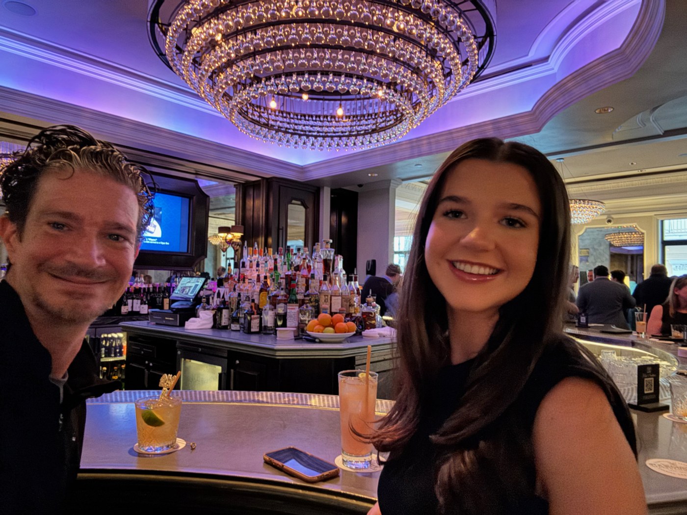 Erik and Maddie seated at a hotel bar beneath a large chandelier in New Orleans