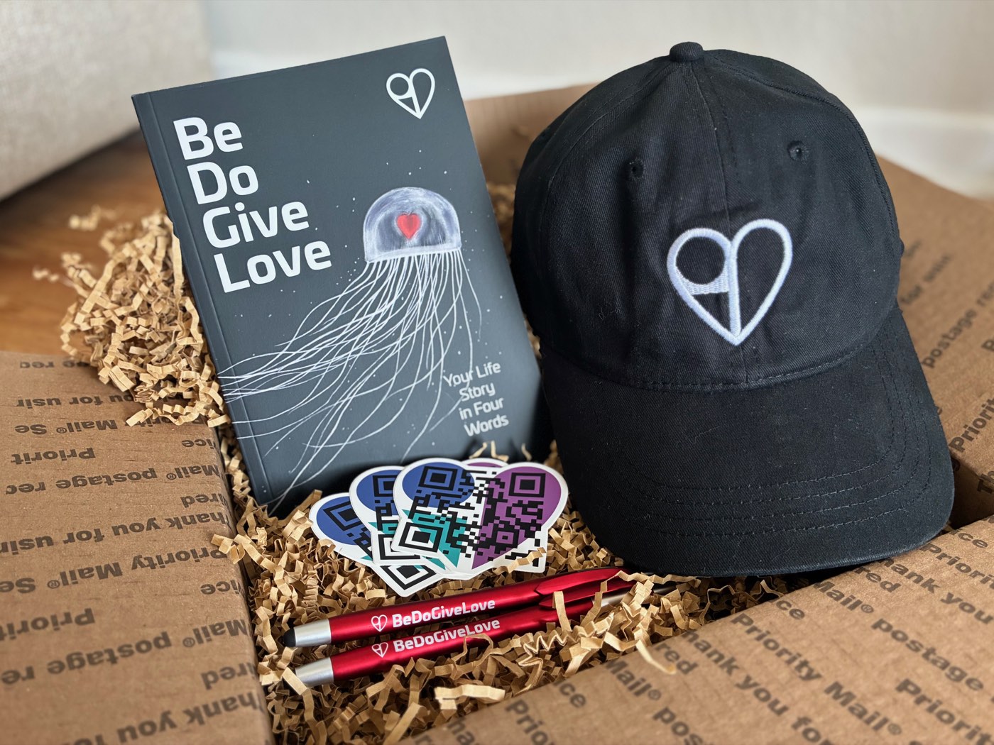 Be Do Give Love paperback gift box: signed book, embroidered hat, sticker pack, and pens